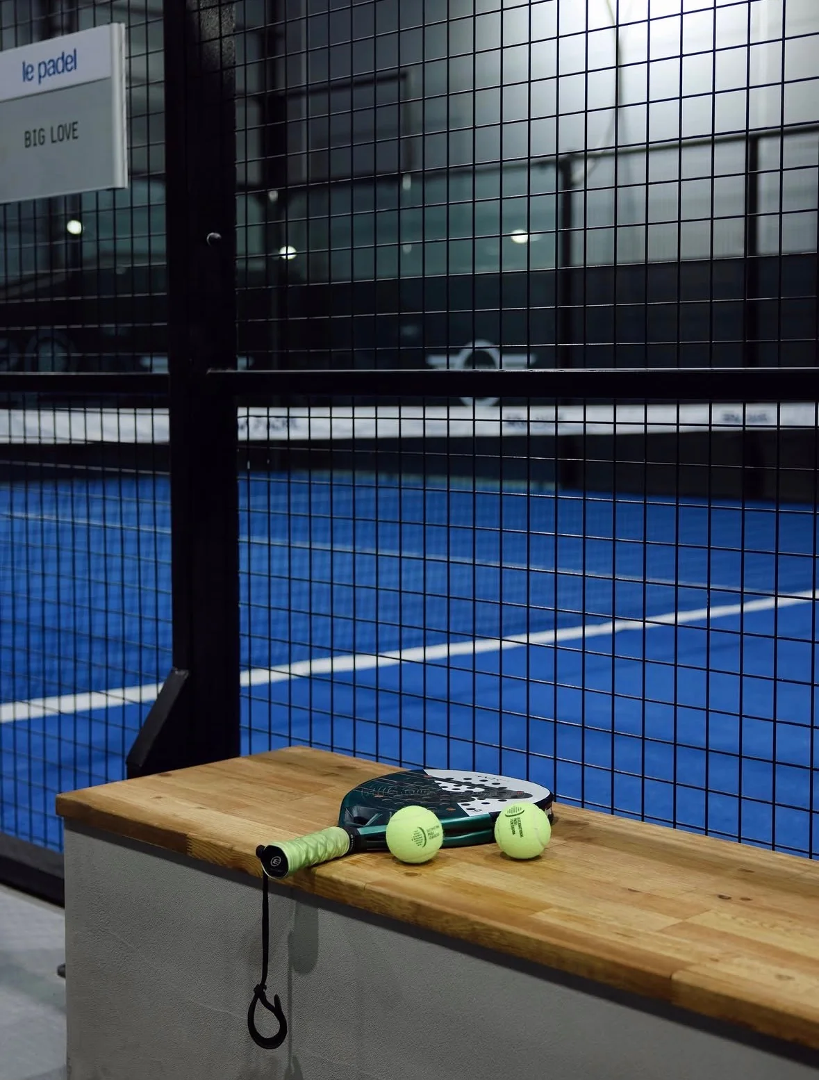 Mavi kort üzerinde fileye yaslanmış padel raketi